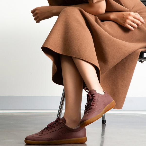Person wearing brown sneakers and a long brown skirt sitting on a chair.