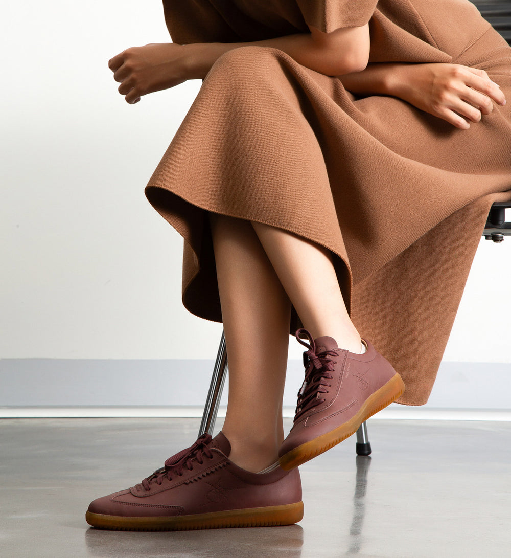 Person wearing brown sneakers and a long brown skirt sitting on a chair.