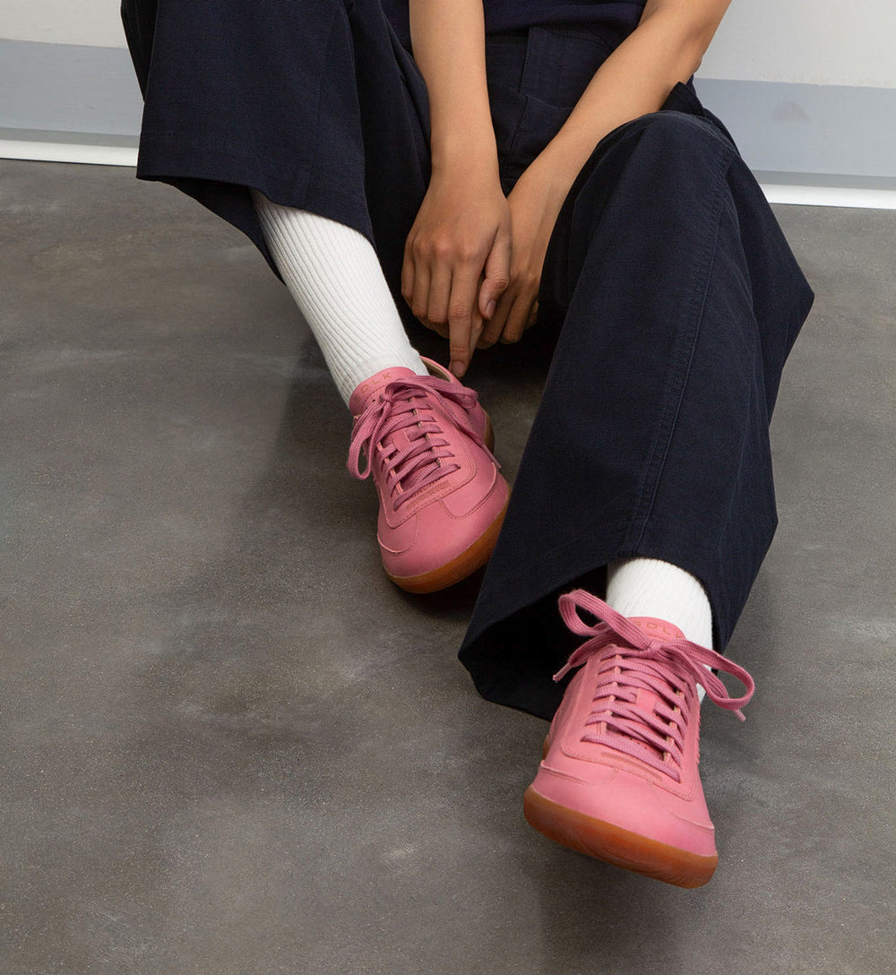 Person wearing pink sneakers with white socks on a gray floor.