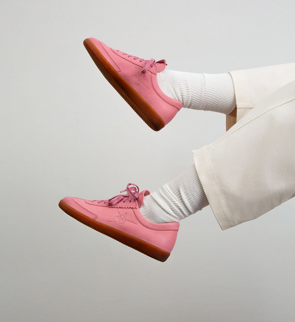 Pink sneakers with brown soles worn by a person on a light gray background