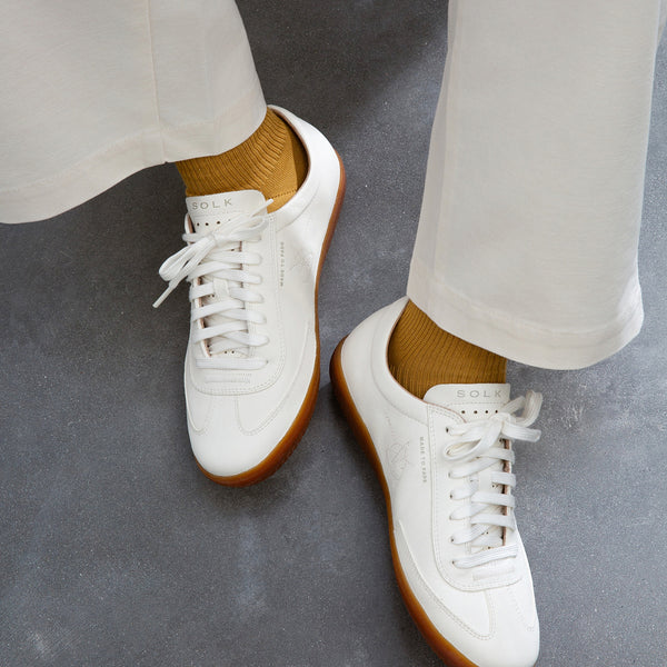 White sneakers with brown soles worn with white pants on a gray surface