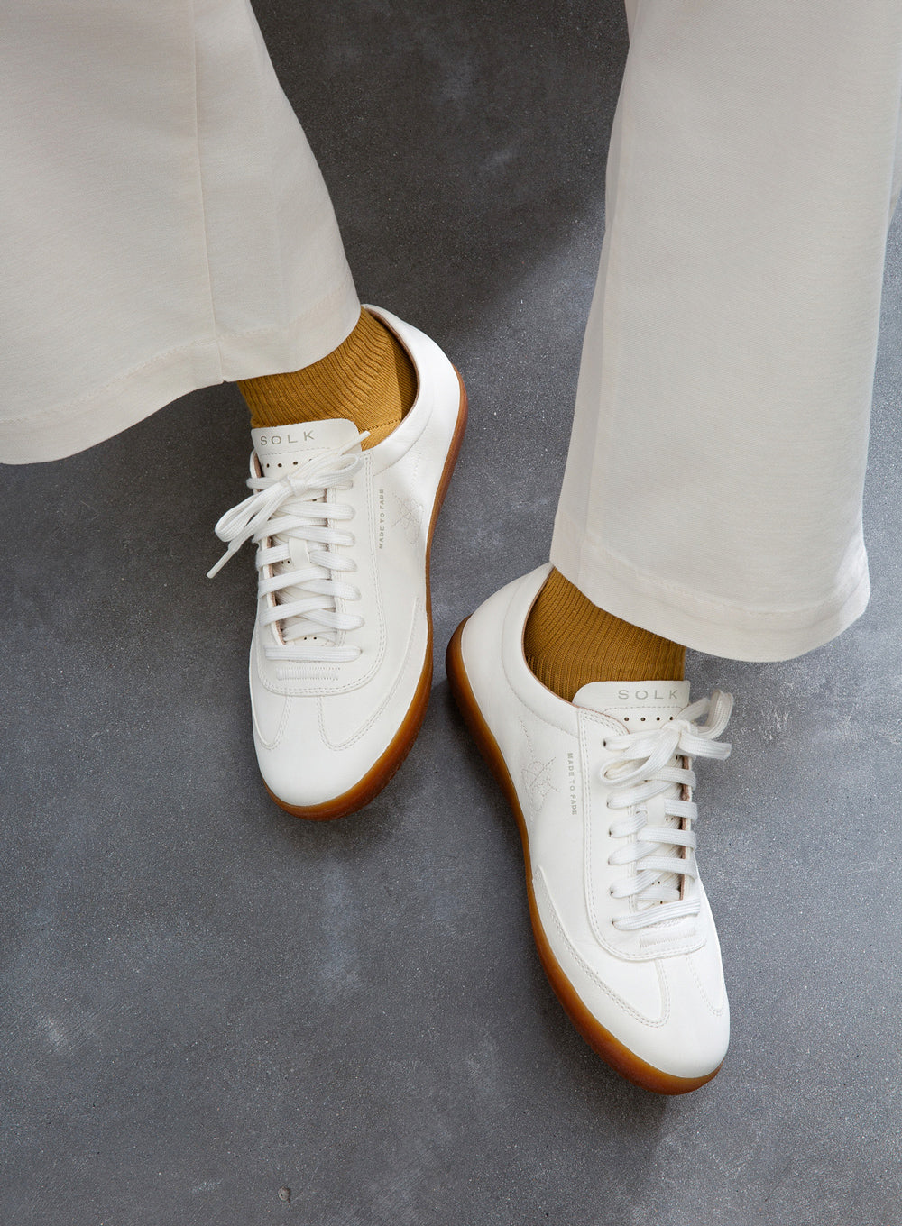 White sneakers with brown soles worn with white pants on a gray surface