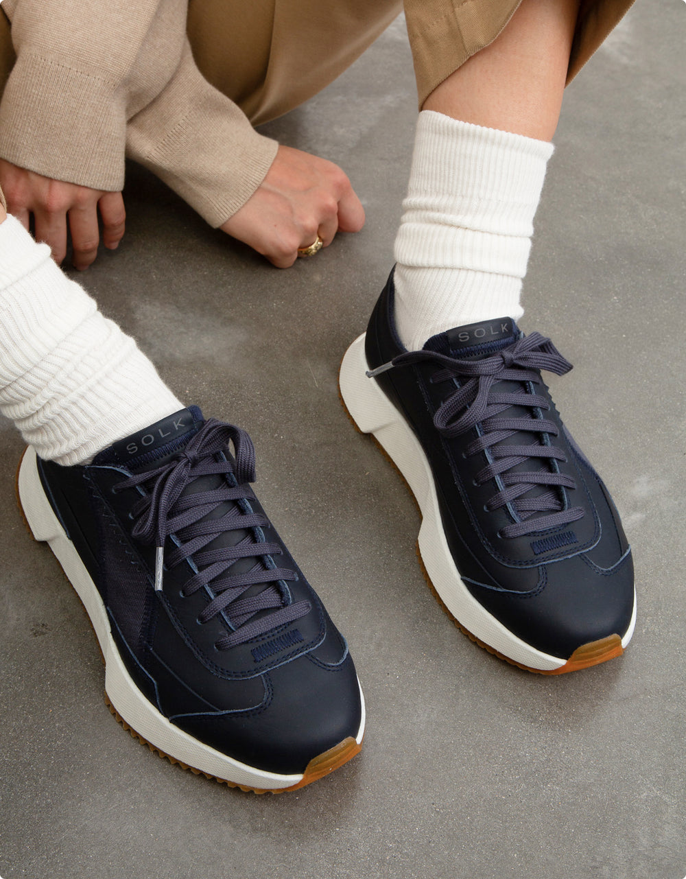 Navy sneakers with white soles worn by a person on a concrete floor.
