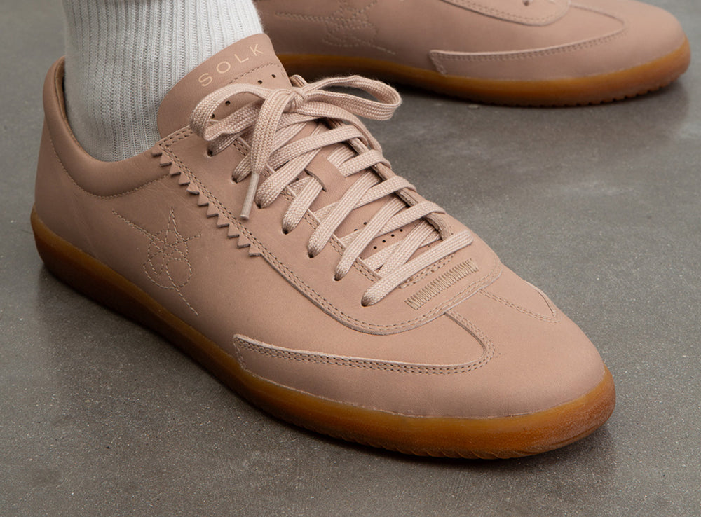 Beige sneaker with brown sole on a concrete floor