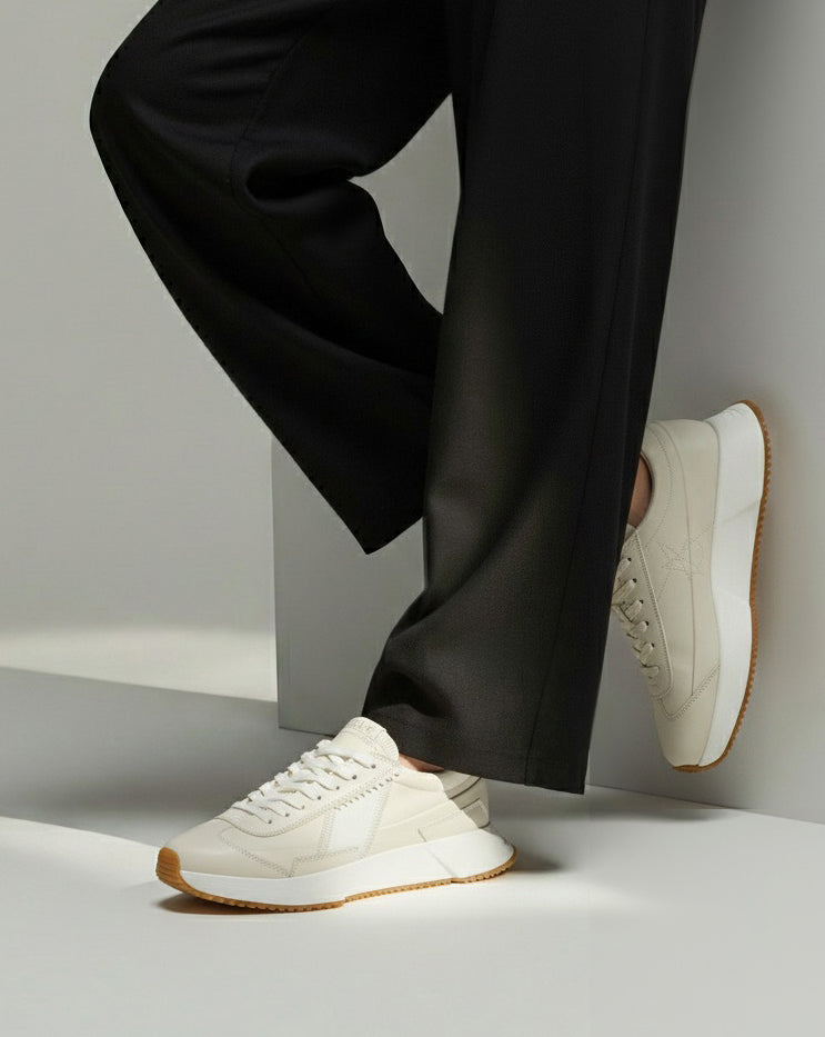 White sneakers with brown soles worn with black pants on a light gray background