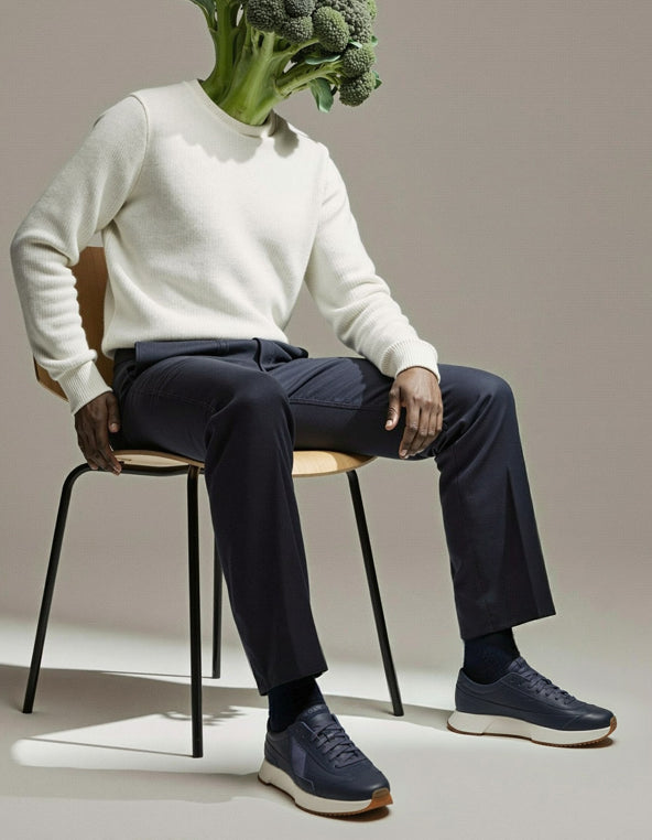 Person wearing a white sweater and dark pants sitting on a chair with a broccoli head.