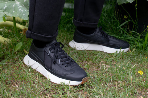 Black sneakers with white soles worn on grass