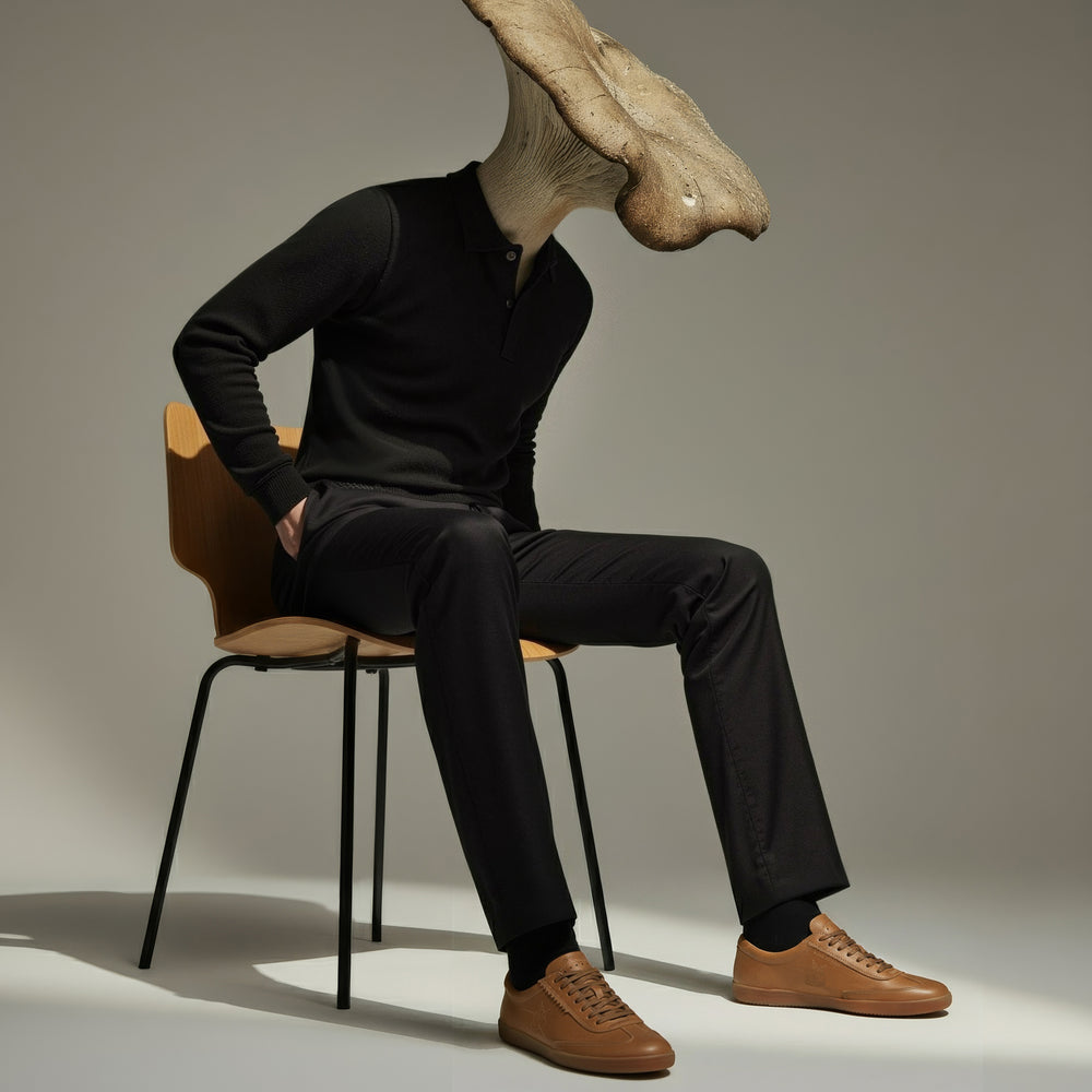 Person wearing a black outfit with a large mushroom head sitting on a chair.