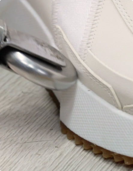 Close-up of a white shoe with brown sole on a light-colored floor.