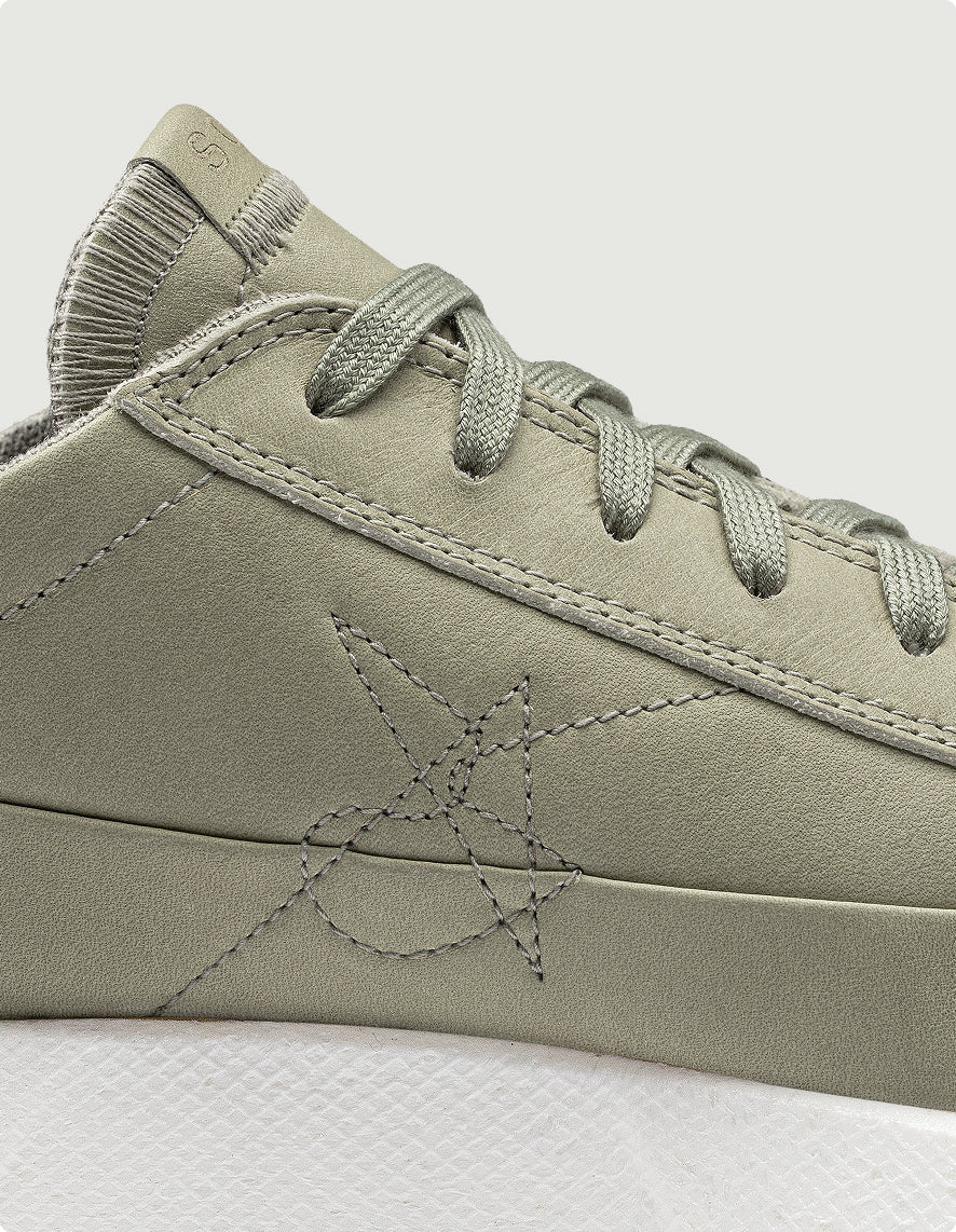 Close-up of a green sneaker with a brand logo on a light gray background