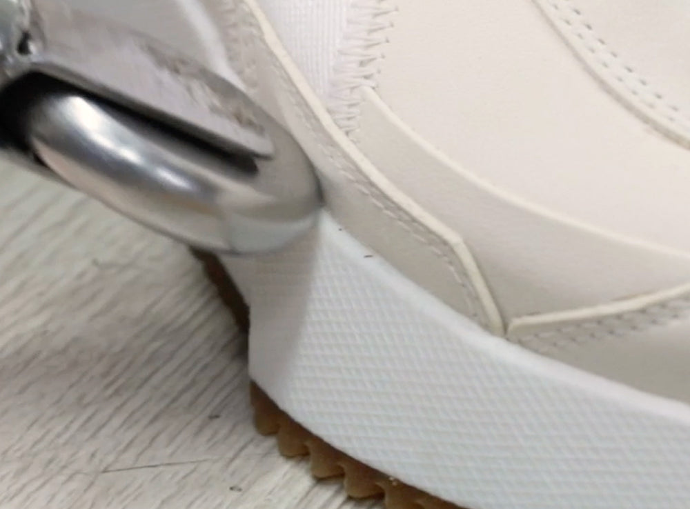 Close-up of a white shoe with a metal object on a wooden floor