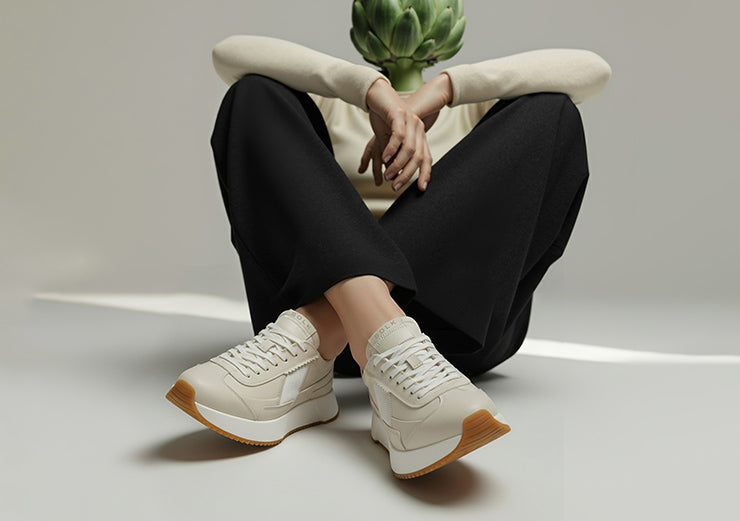 Person wearing white sneakers with brown soles sitting on a light gray floor.